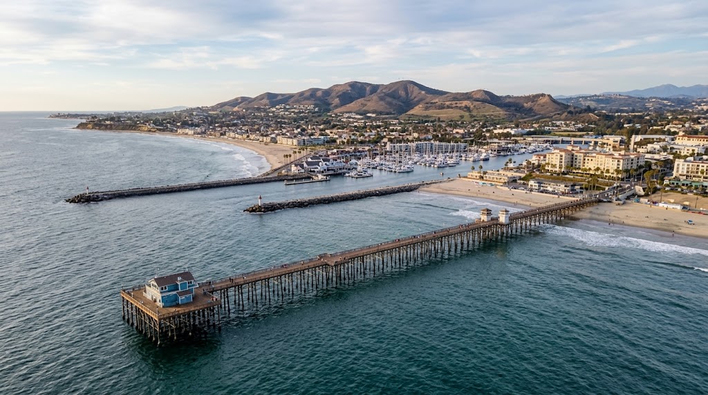 Wide coastal shot of Oceanside (pier or harbor) with the hills of North County behind.